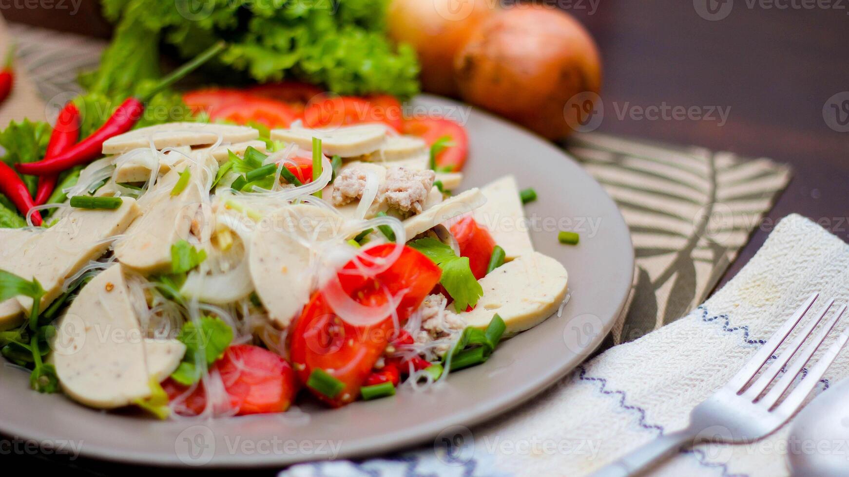 kryddad glas nudel sallad med vietnamese korv eras i en grå tallrik sätta på en trä- tabell och olika grönsaker. foto