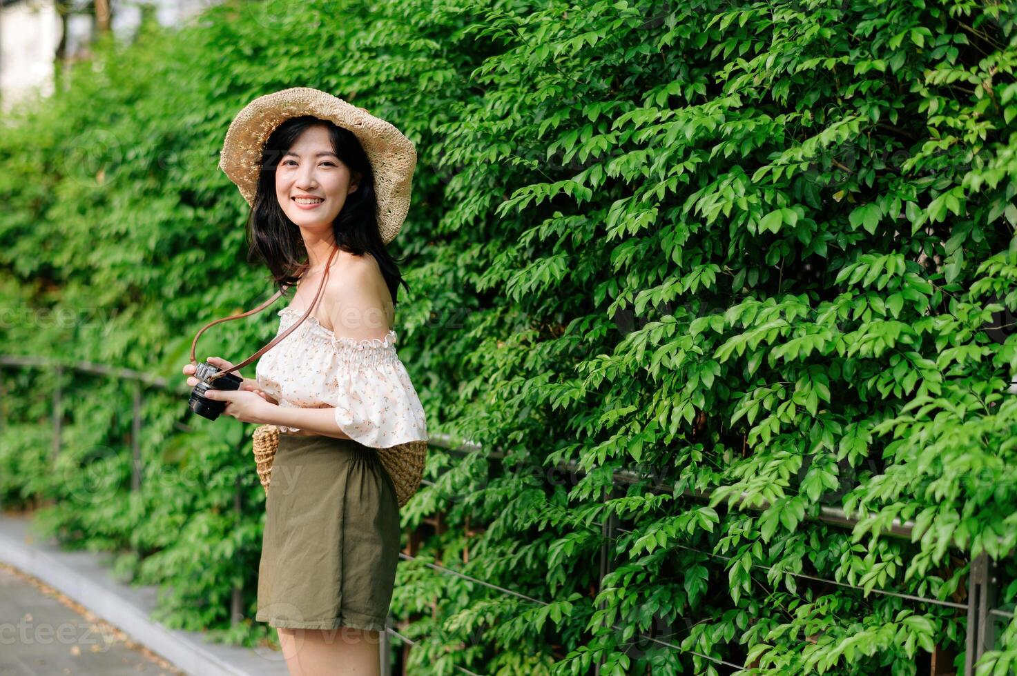 porträtt av asiatisk ung kvinna resande med vävning hatt och korg och en kamera på grön offentlig parkera natur bakgrund. resa resa livsstil, värld resa explorer eller Asien sommar turism begrepp. foto