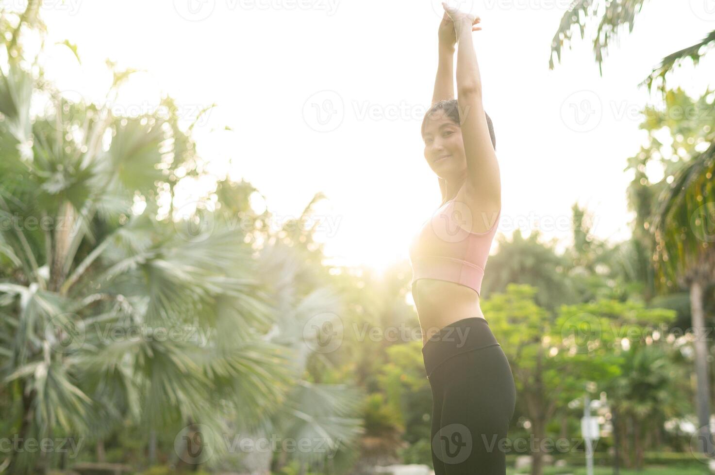 wellness och välbefinnande passa 30s ung asiatisk kvinna i rosa sportkläder engagerar i yoga och sträckor muskler. omfamning en friska utomhus- livsstil med detta kondition yoga flicka i en offentlig parkera på solnedgång. foto