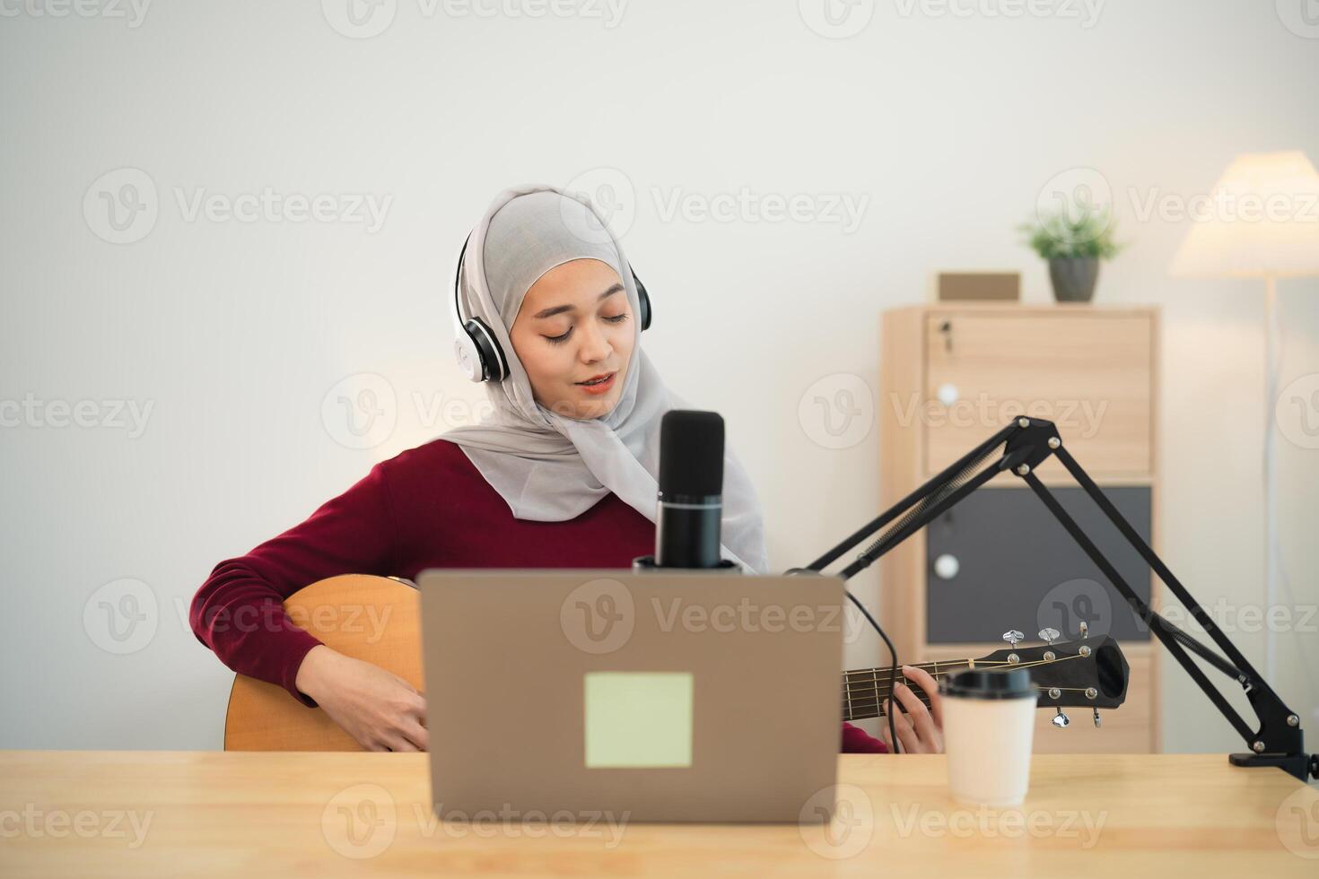 muslim islam kvinna bär hijab leva strömning prestanda spelar gitarr och sjunga en låt. asiatisk kvinnor undervisning gitarr och sång uppkopplad. musiker inspelning musik med bärbar dator spelar akustisk gitarr. foto