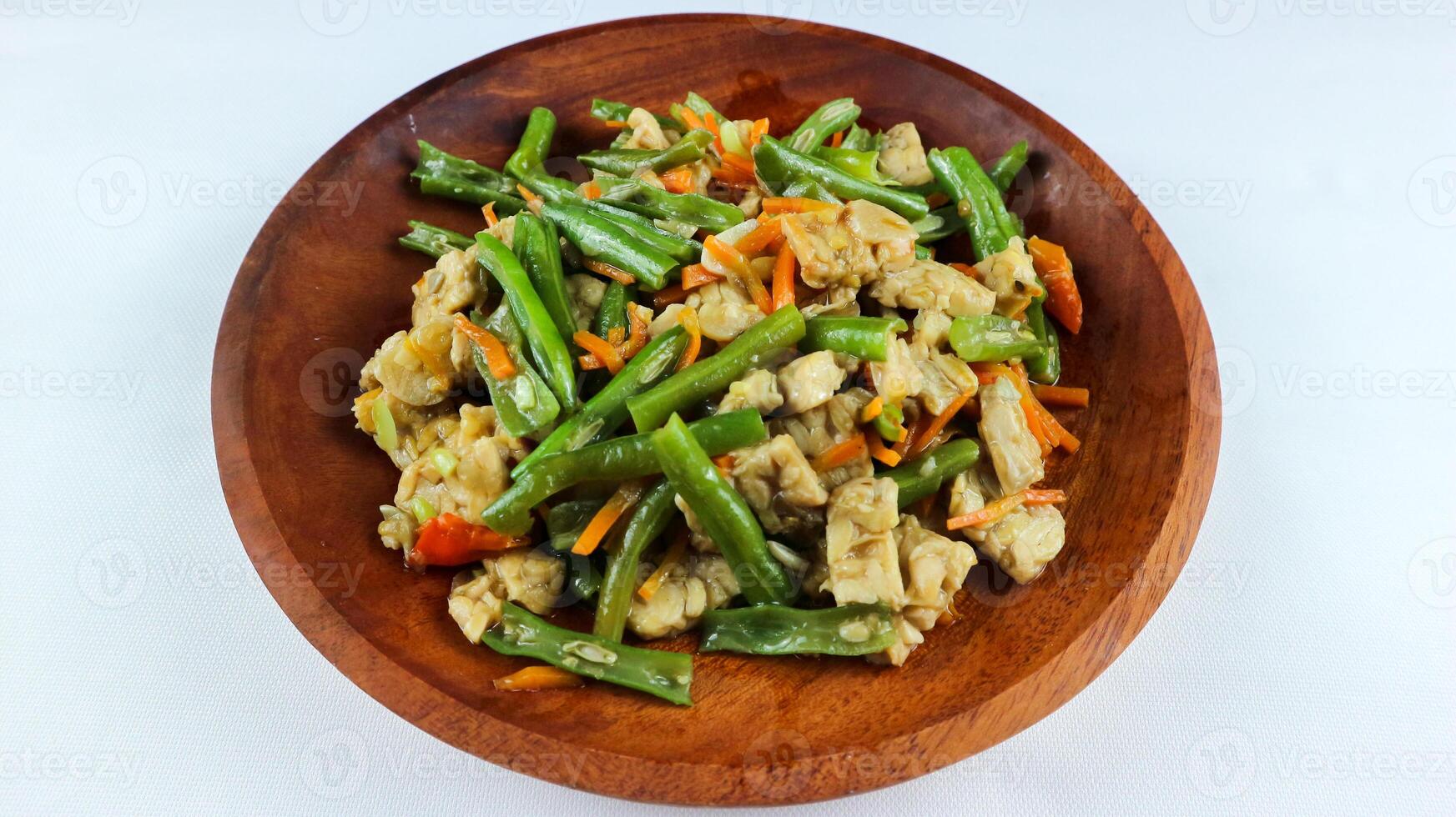 tumis buncis, wortel och tempe eller stek bönor, morötter och tempeh. eras på en trä- tallrik och isolerat på en vit bakgrund. foto