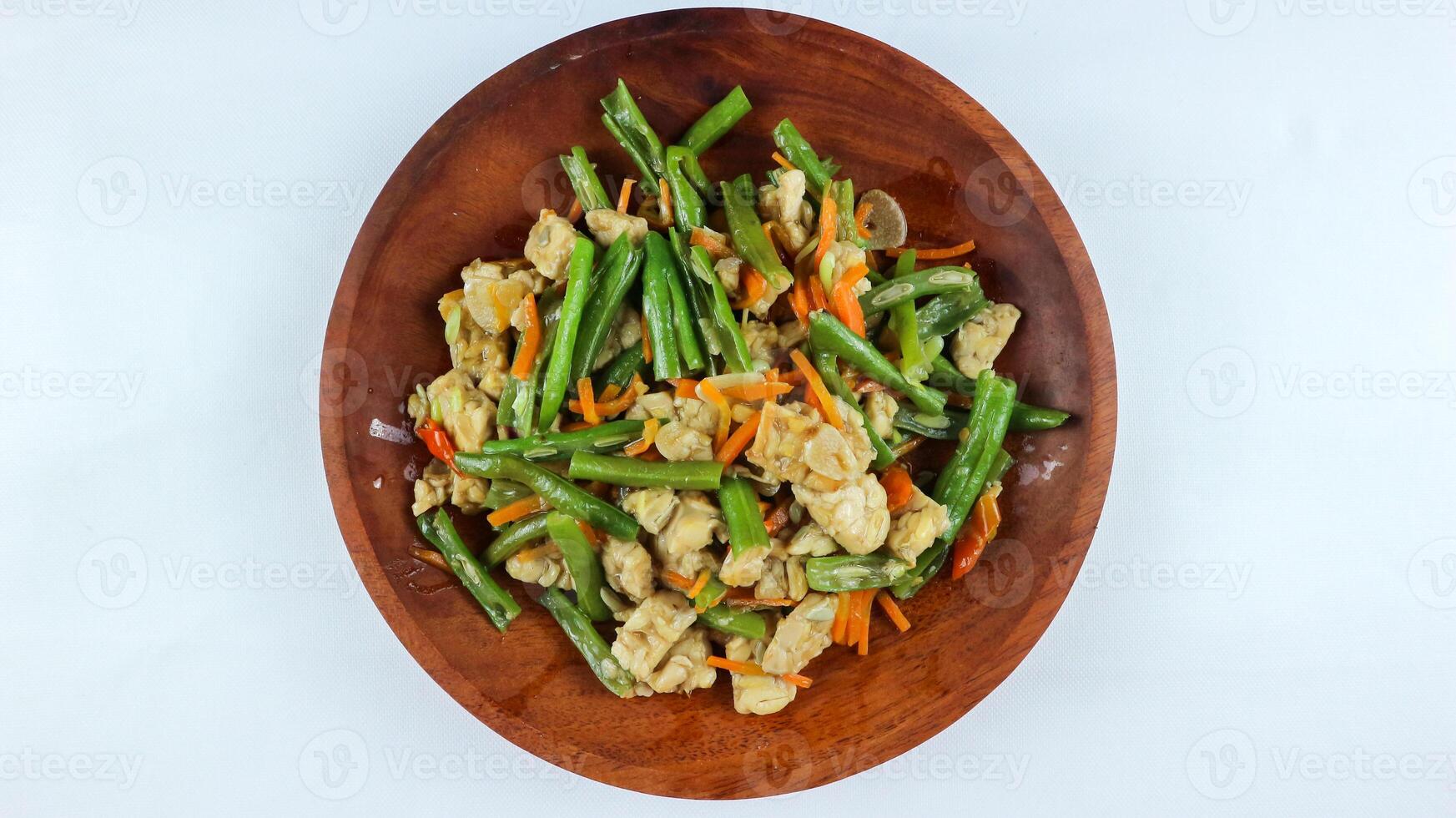 tumis buncis, wortel och tempe eller stek bönor, morötter och tempeh. eras på en trä- tallrik och isolerat på en vit bakgrund. foto