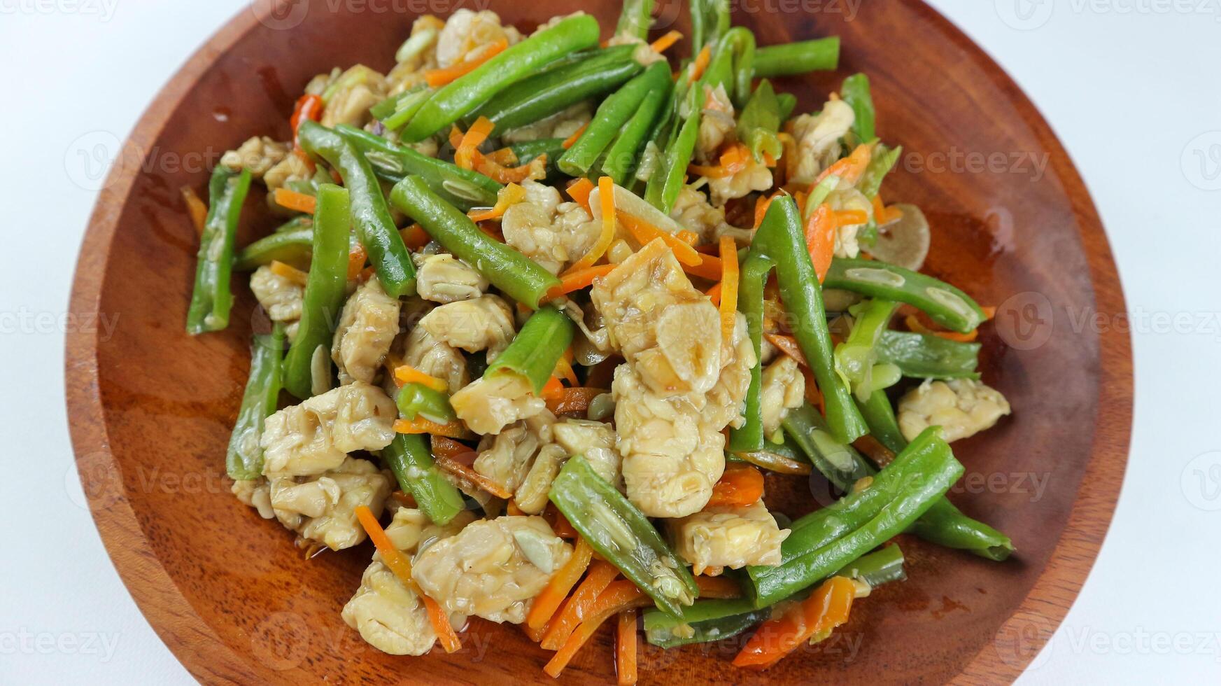 tumis buncis, wortel och tempe eller stek bönor, morötter och tempeh. eras på en trä- tallrik och isolerat på en vit bakgrund. foto