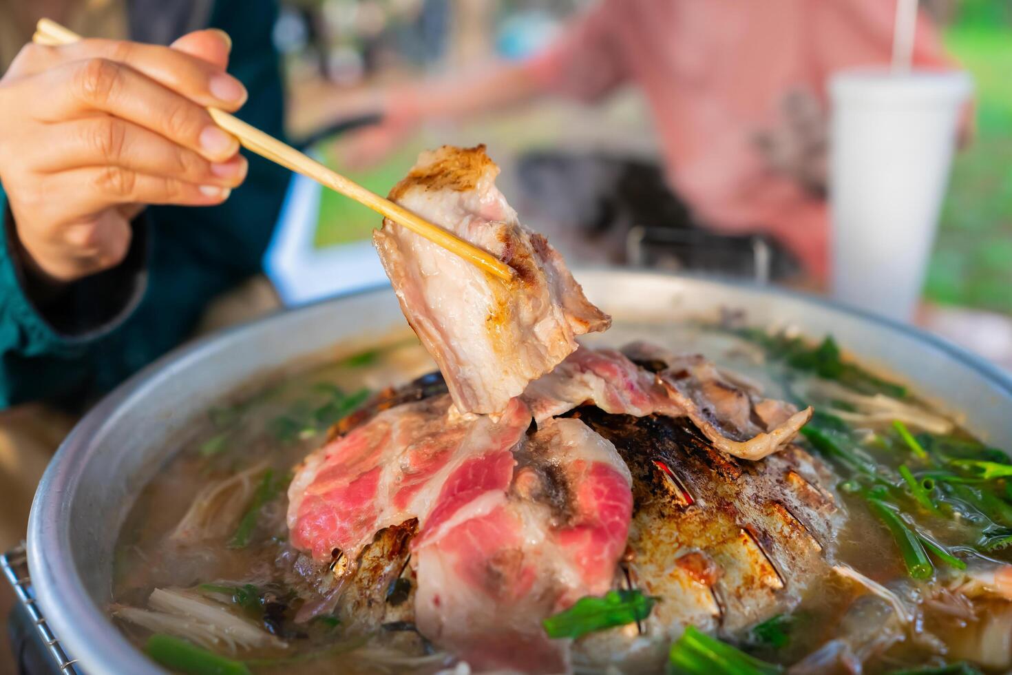 koreanska bbq eller mookata med skivad fläsk och vegetabiliska soppa, människor hand använder sig av ätpinnar grillad middag de familj. picknick utomhus. stänga upp foto