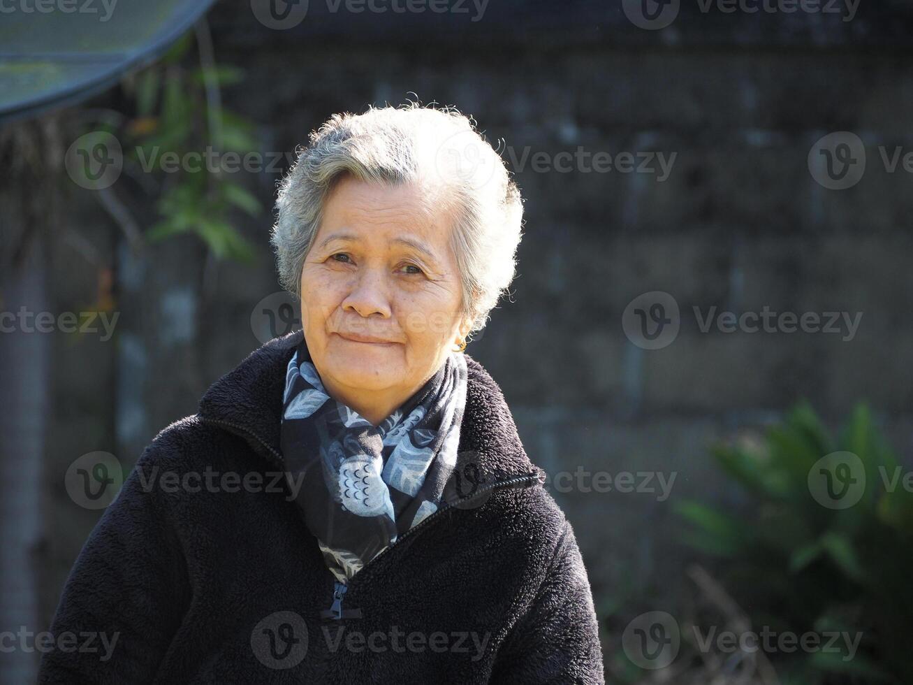 porträtt av en skön äldre kvinna leende och ser på de kamera medan stående i en trädgård. foto
