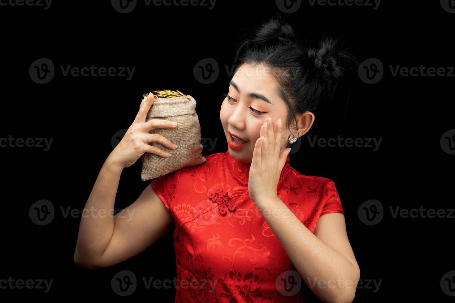 porträtt asiatisk ung, kvinna röd klänning traditionell cheongsam som håller ett guldmynt i en säck på den svarta bakgrunden foto