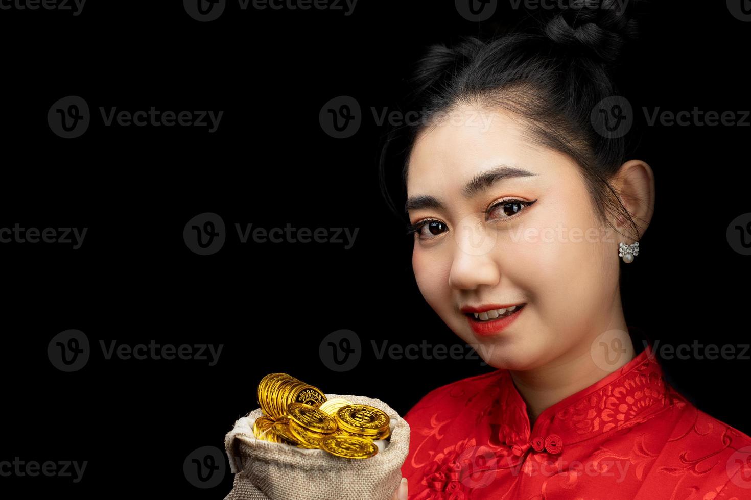 porträtt asiatisk ung, kvinna röd klänning traditionell cheongsam som håller ett guldmynt i en säck på den svarta bakgrunden foto