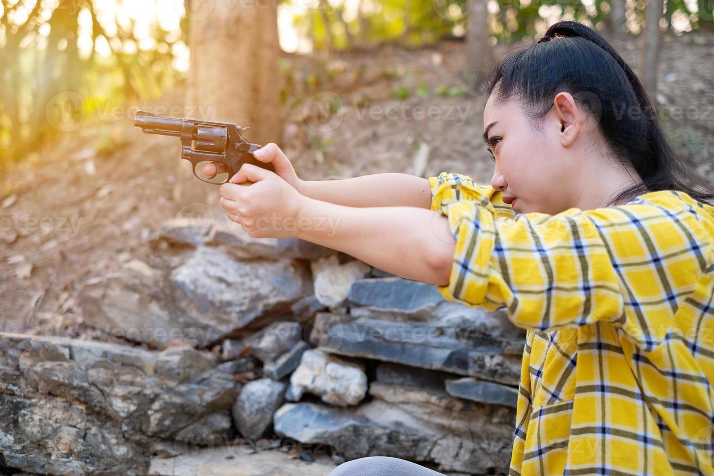 porträtt bonden asea kvinna klädd i en skjorta vid skottet från en gammal revolverpistol på gården, ung flicka sitter i attityden att sikta och titta genom siktet pistol foto