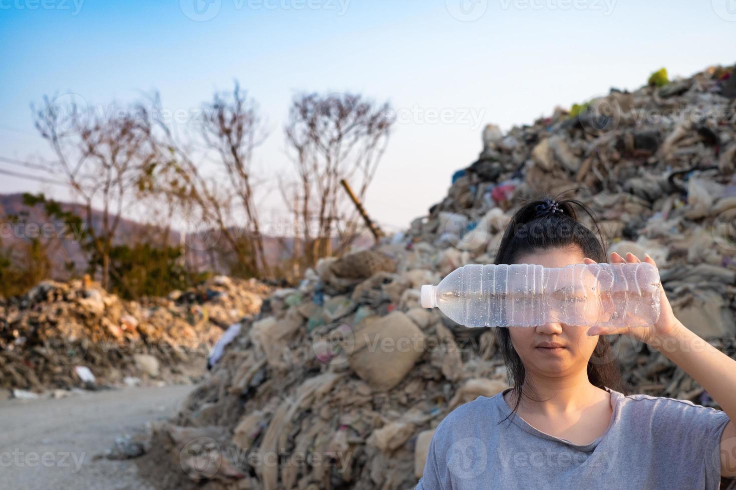 kvinna hand som håller använda en klar plastflaska för att täcka ansiktet på berget stora sopor bakgrund foto