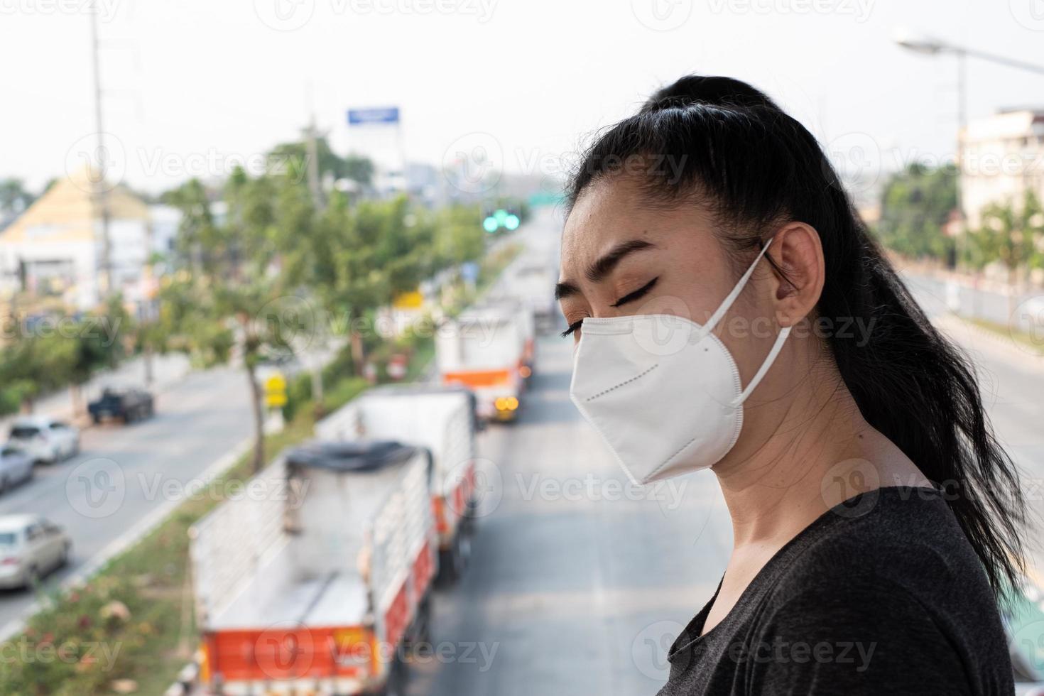 närbild av en kvinna som står och sätter på sig en respirator n95-mask för att skydda mot luftburna luftvägssjukdomar när influensa covid-19 coronavirus ebola pm2.5 damm och smog på vägen burrade bakgrunden foto