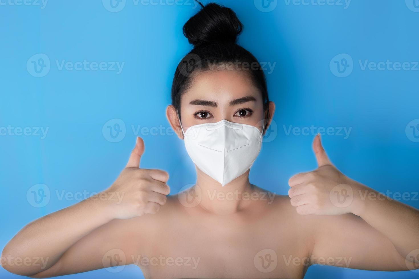 närbild av en kvinna som sätter på sig en respirator n95-mask för att skydda mot luftburna luftvägssjukdomar som influensa covid-19 corona pm2.5 damm och smog, kvinnlig tummen upp gest med handen foto