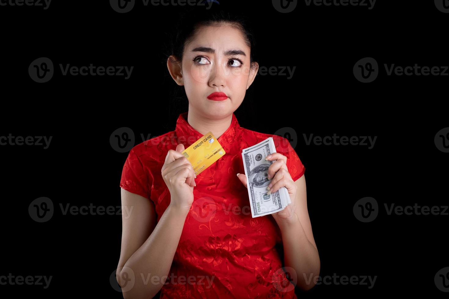 porträtt av en vacker ung asiatisk kvinna röd klänning traditionell cheongsam som håller kreditkort och pengar sedel 100 usd på den svarta bakgrunden foto