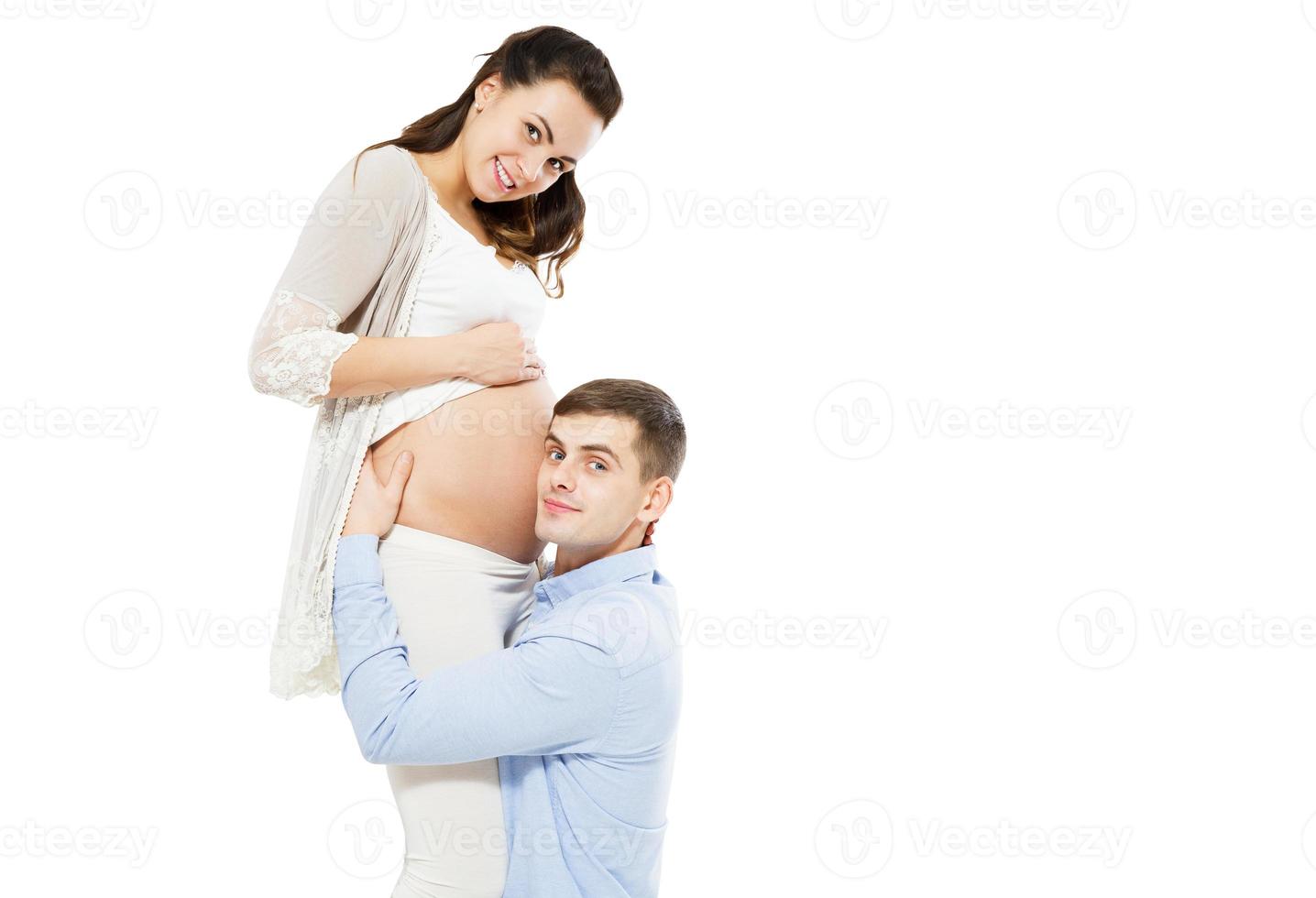 ung man lyssnar på sin frus gravida mage på en vit bakgrund, kvinna graviditet foto