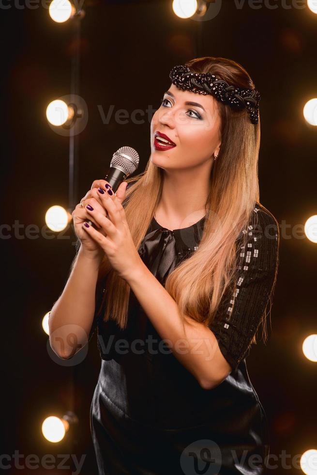 ung smiley vacker långt hår flicka med mikrofon sjunger sång på scenen i karaoke foto