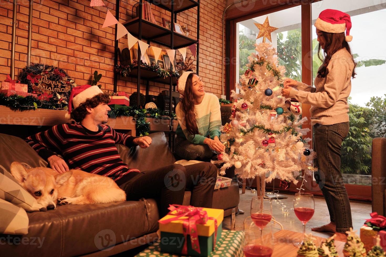 familj med hund och vänner tillsammans dekorerar glatt den vita julgranen i hemmets vardagsrum, roligt och glad förbereder sig för en fest för nyårsfesten. foto