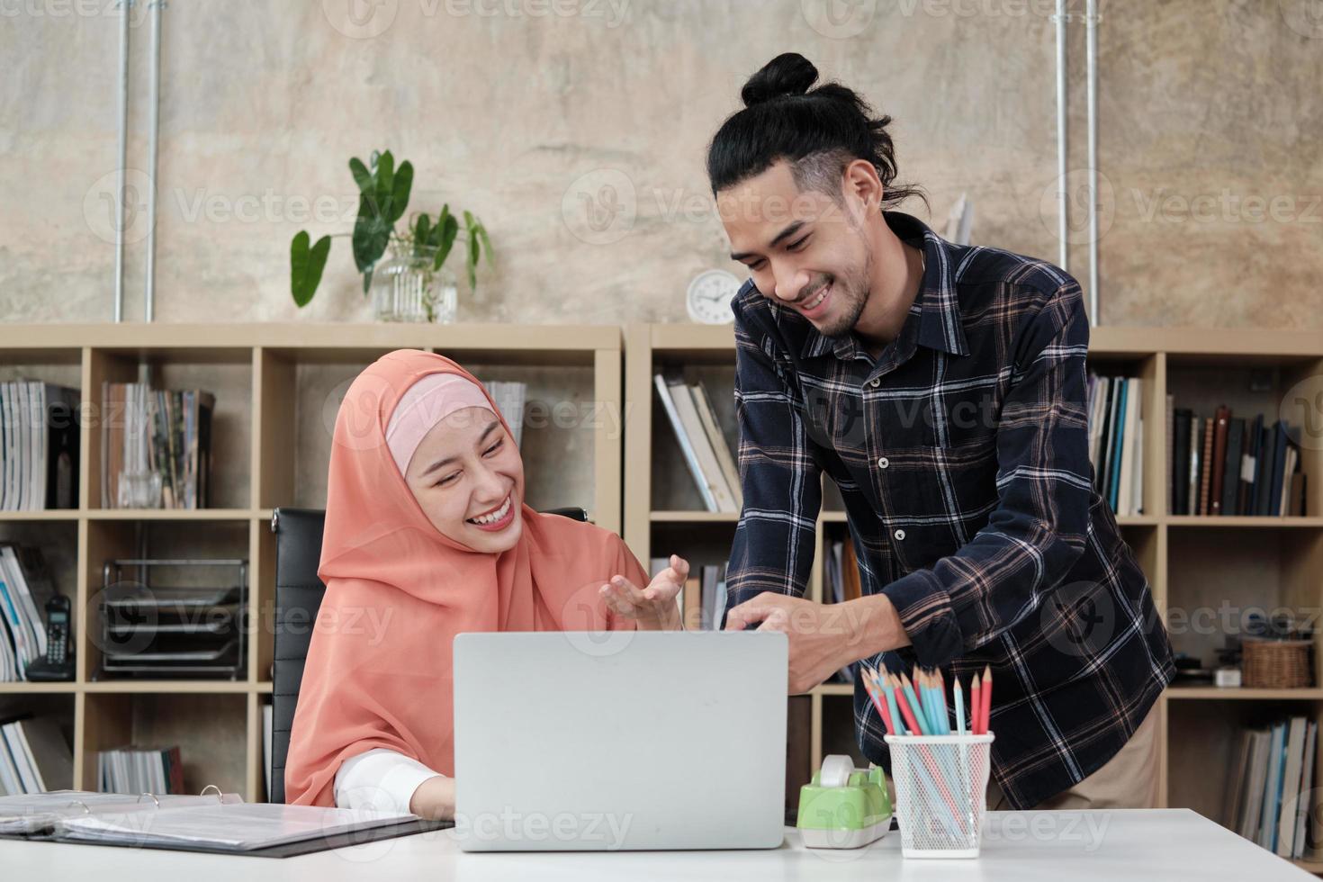 två unga startkollegor som är islamiska människor pratar om framgång med att arbeta i en e-handelsverksamhet med ett leende. använda bärbar dator till online -kommunikation via internet på ett litet kontor. foto
