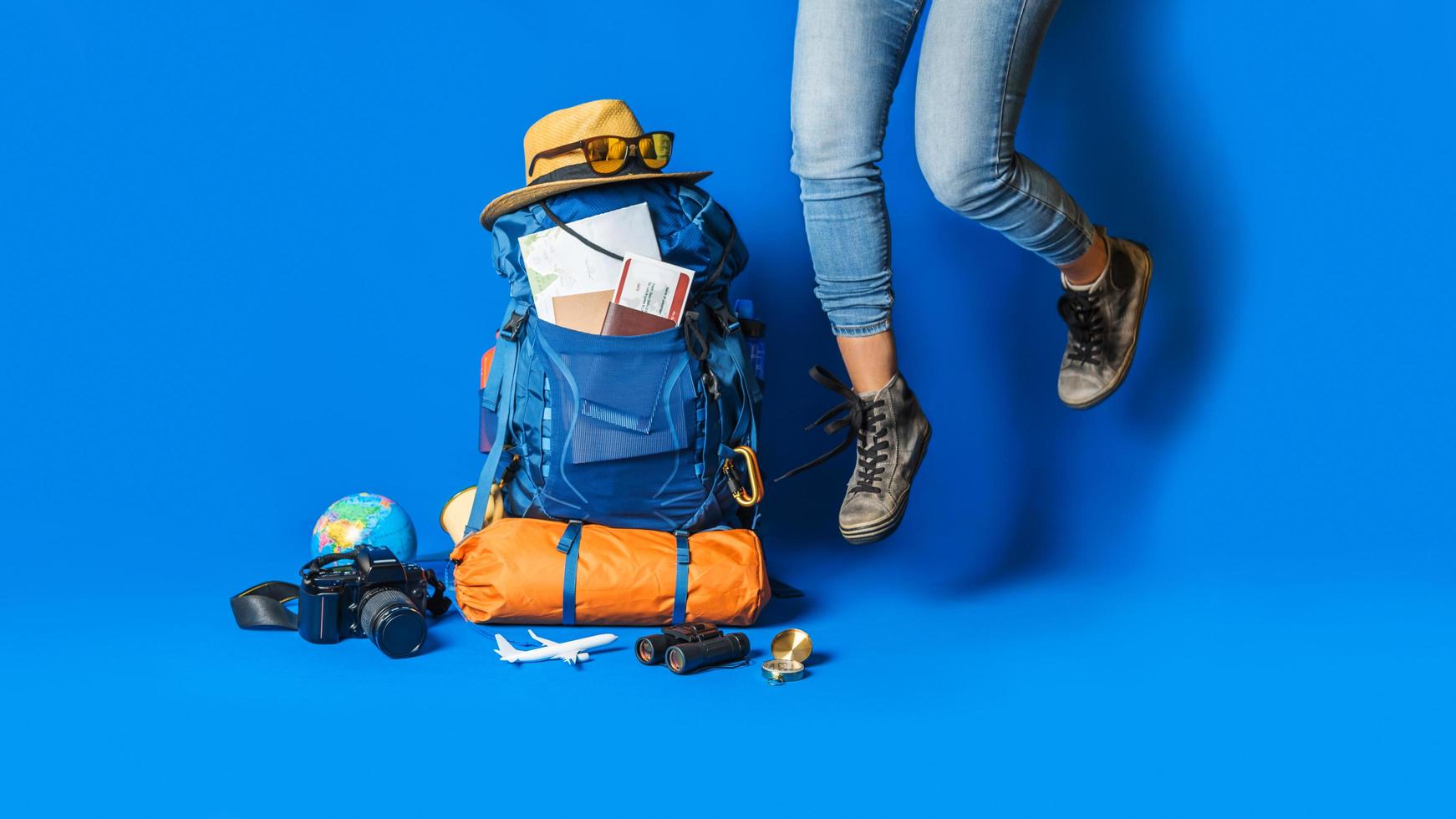 turistplaneringssemester med hjälp av världskartan med andra resetillbehör runt om. kvinna resenär med resväska på blå färg bakgrund. koncept reseryggsäck foto