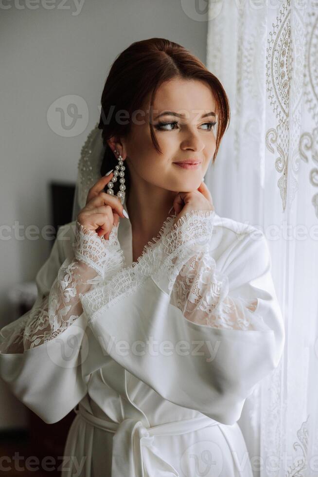 en skön brunett brud med en tiara i henne hår är få redo för de bröllop i en skön morgonrock i budoar stil. närbild bröllop porträtt, Foto. foto