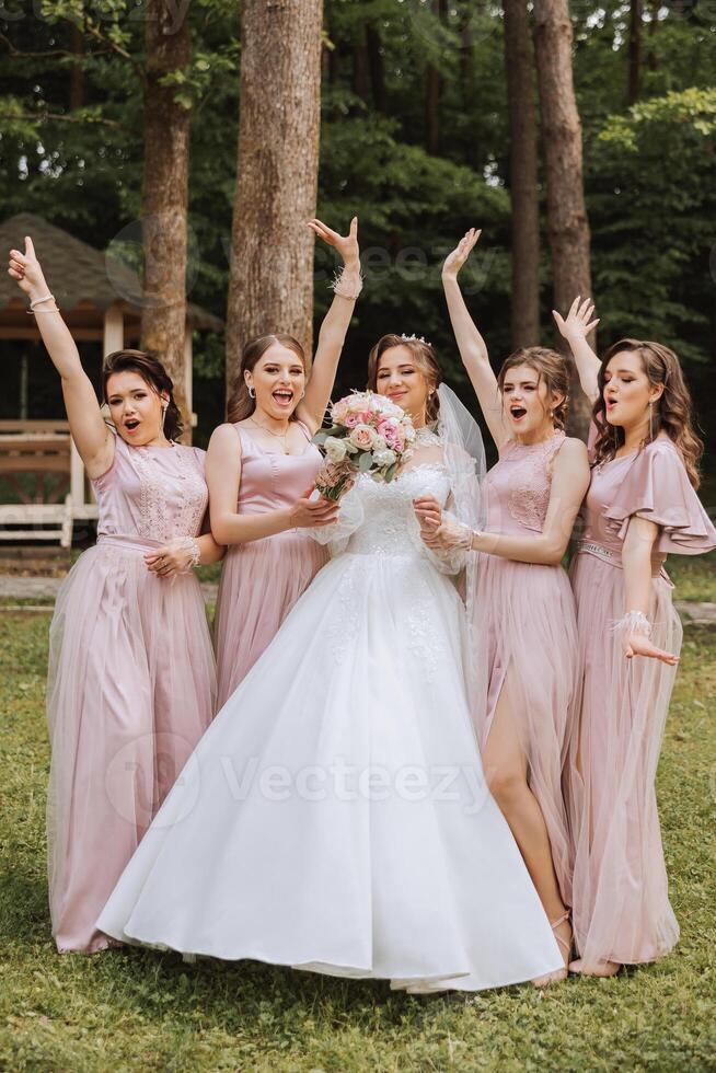 grupp porträtt av de brud och tärnor. brud i en bröllop klänning och brudtärnor i rosa eller pulver klänningar och innehav eleganta buketter på de bröllop dag. foto