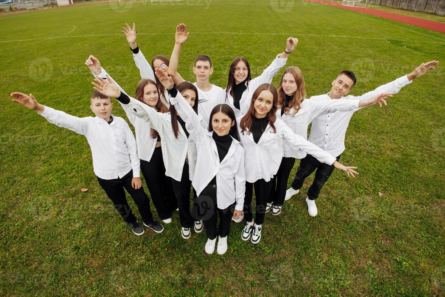 en grupp av många Lycklig tonåringar klädd i de samma utrusta har roligt och Framställ i en stadion nära en högskola. begrepp av vänskap, stunder av lycka. skola vänskap foto