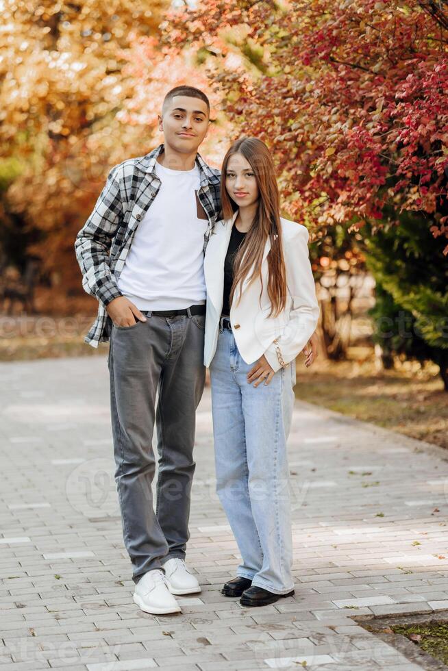 vertikal Foto av två Tonårs vänner klädd i tillfällig kläder stående Nästa till varje Övrig mot en bakgrund av natur. bäst skola vänner är redo till betagen något till uppnå de mål.