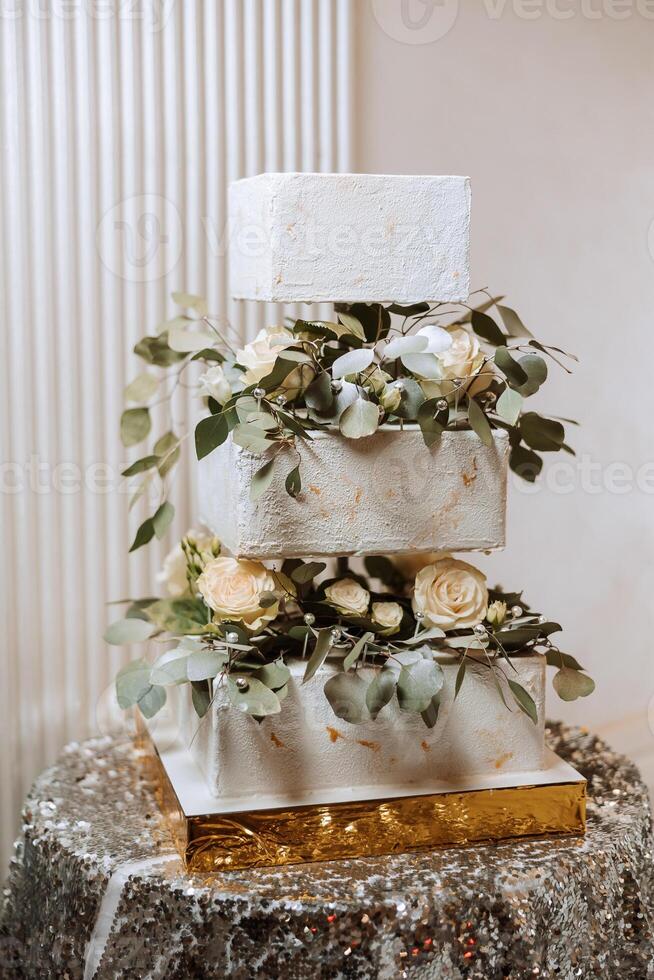 en stor lyxig flerdelad bröllop kaka är dekorerad med färsk blommor av vit ro och eukalyptus löv i de bankett hall. bröllop efterrätt under de kväll ljus. bröllop dekor. foto