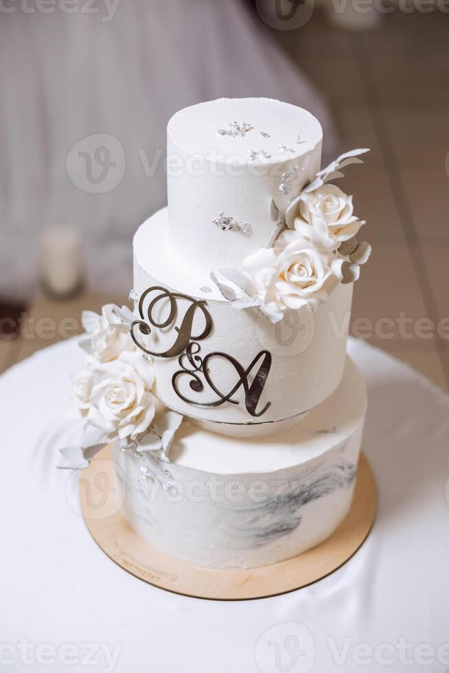 en stor lyxig flerdelad bröllop kaka är dekorerad med färsk vit reste sig blommor i de bankett hall. bröllop efterrätt under de kväll ljus. bröllop dekor. foto