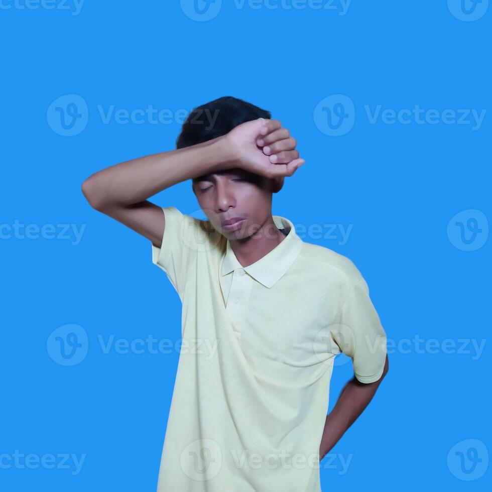ung asiatisk man gråt innehav både nävar över ögon, bär blå skjorta. isolerat blå bakgrund. foto