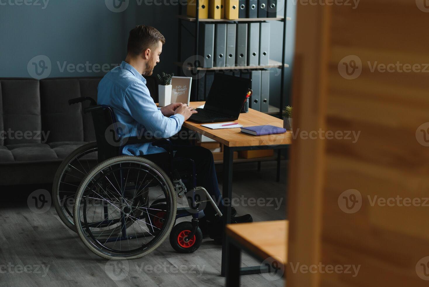 ung man med särskild behov i tillfällig kläder arbetssätt på trådlös bärbar dator. manlig frilansare arbetssätt från Hem medan Sammanträde i rullstol foto