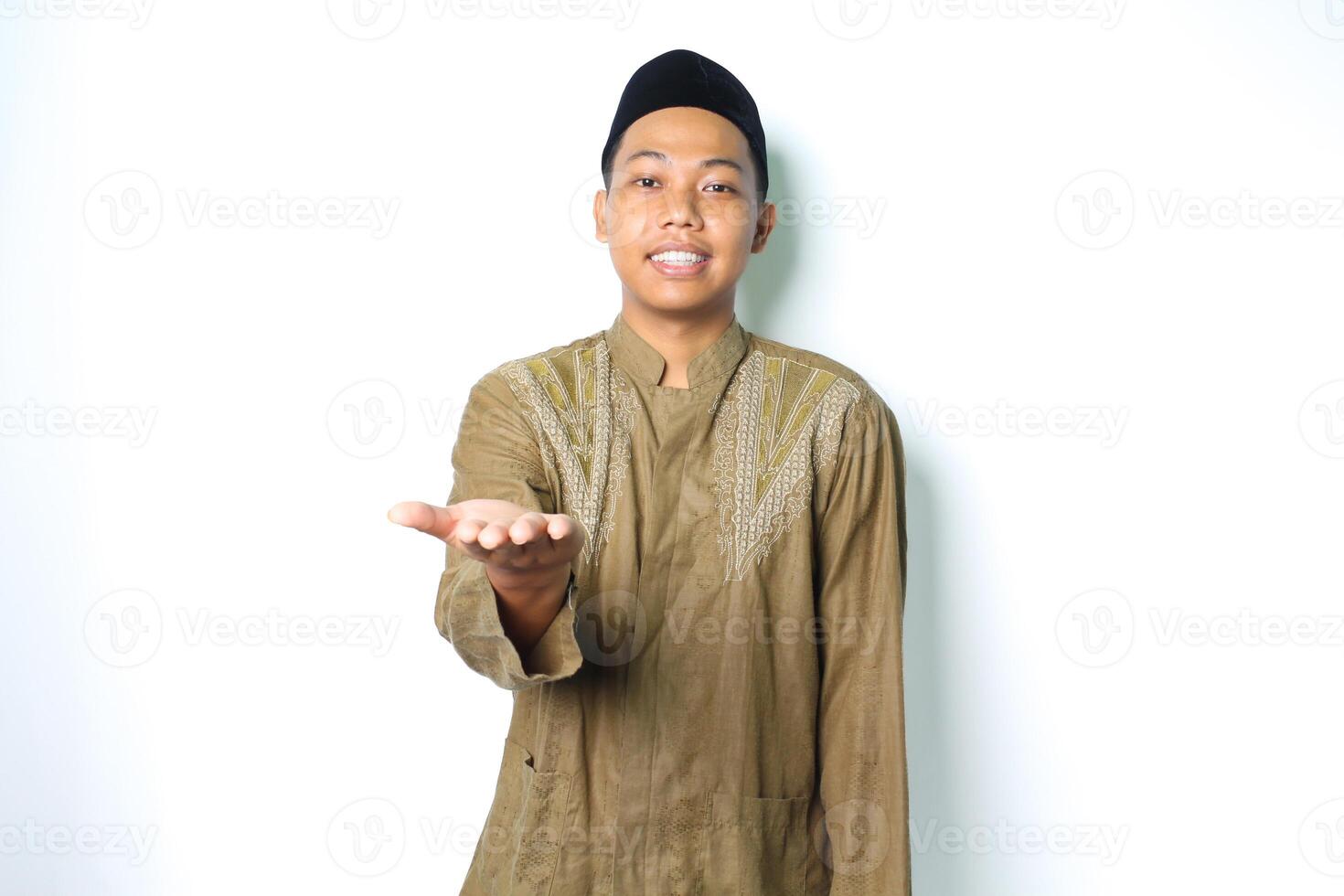 leende asiatisk muslim man bär islamic klänning presenter med öppen handflatan på kamera isolerat på vit bakgrund foto