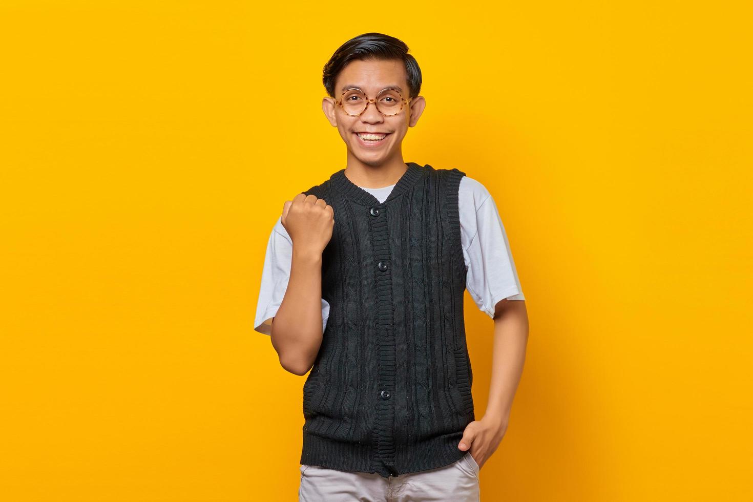 porträtt av upphetsad ung asiatisk man som firar framgång med upphöjda armar på gul bakgrund foto