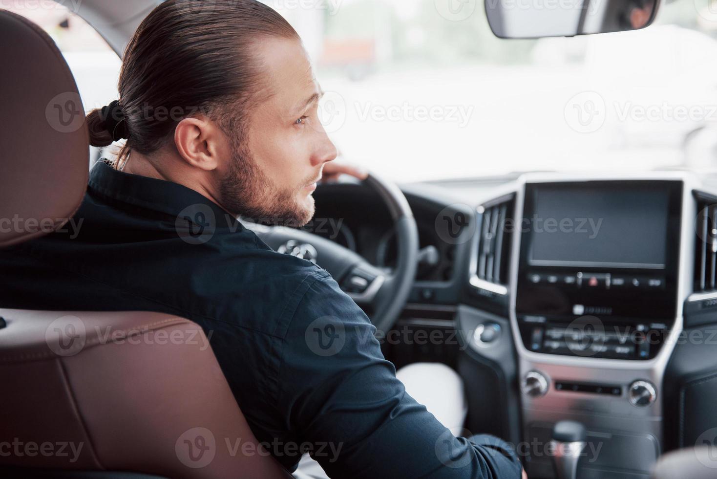 självsäker ung affärsman sitter vid ratten i sin nya bil foto