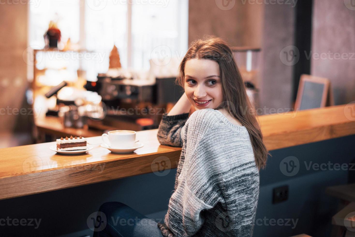 glad leende ung kvinna som använder telefonen i ett café. vacker tjej i trendiga vårfärger foto