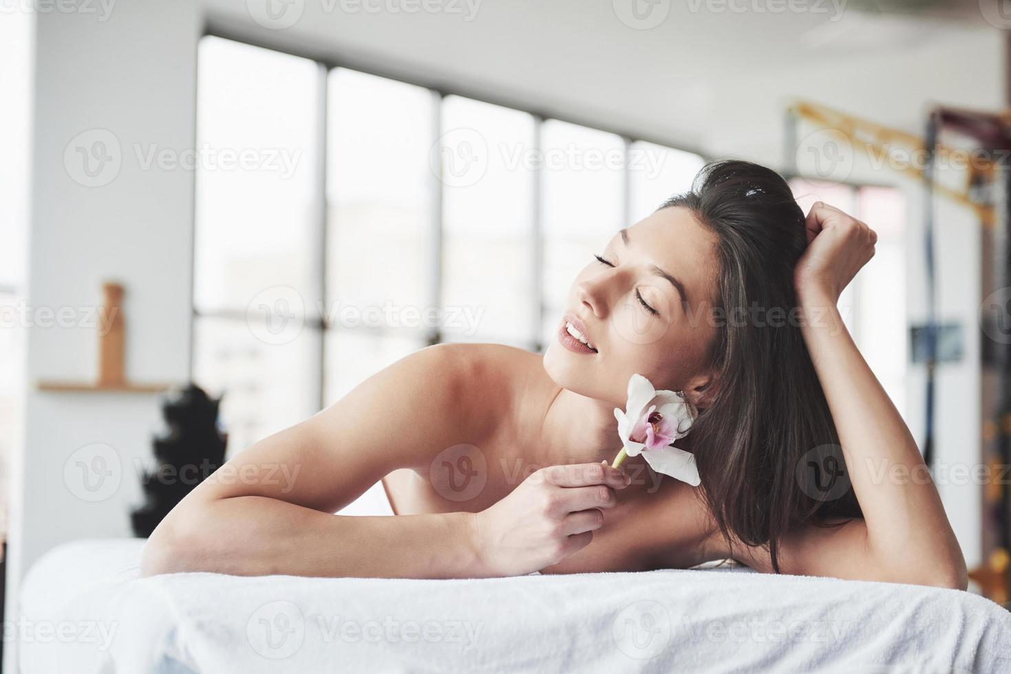 en vacker ung kvinna som kopplar av med en orkidéblomma, framför en massage. foto