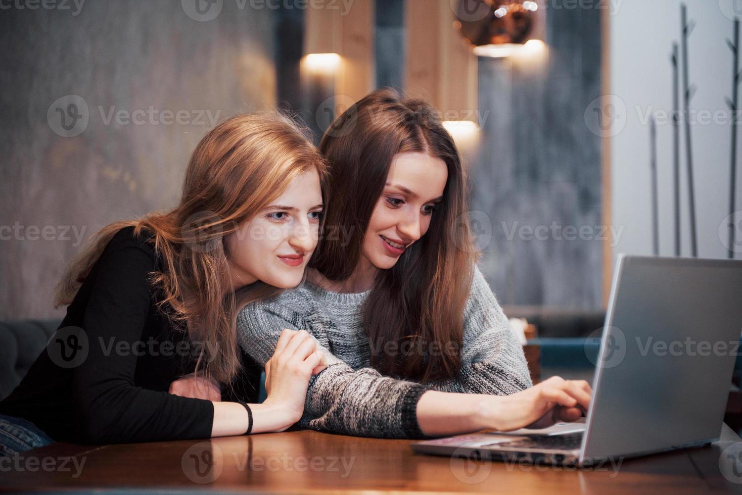 två tjejer som surfar på nätet, gör inlägg på sociala nätverk på en bärbar dator och har roligt foto