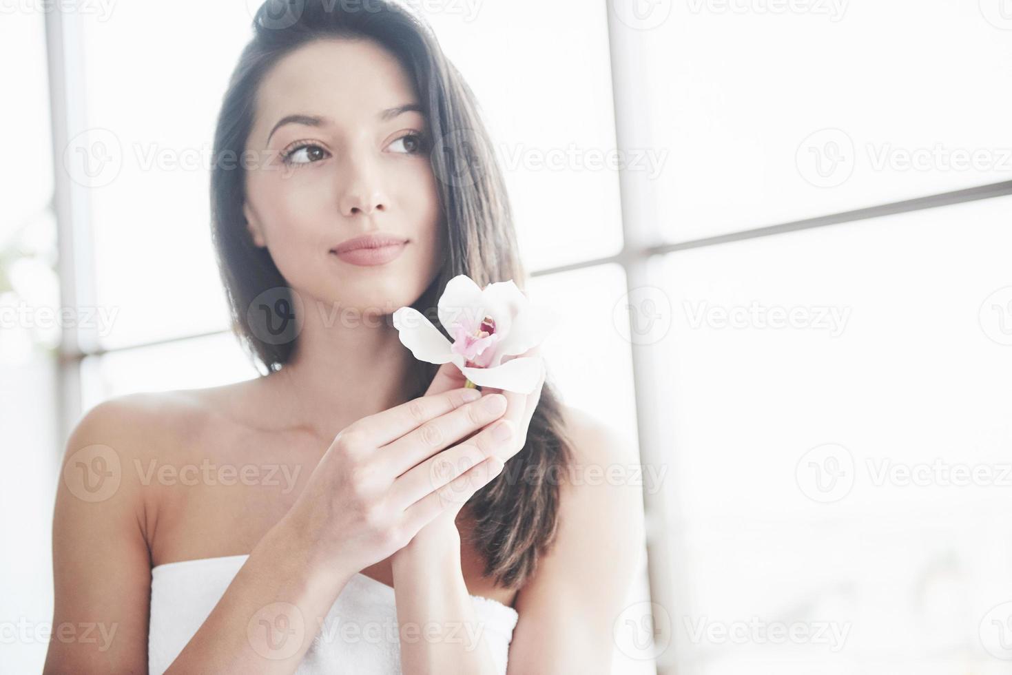 vacker flicka i en handduk med en orkidé, avslappningsmassage väntar. foto
