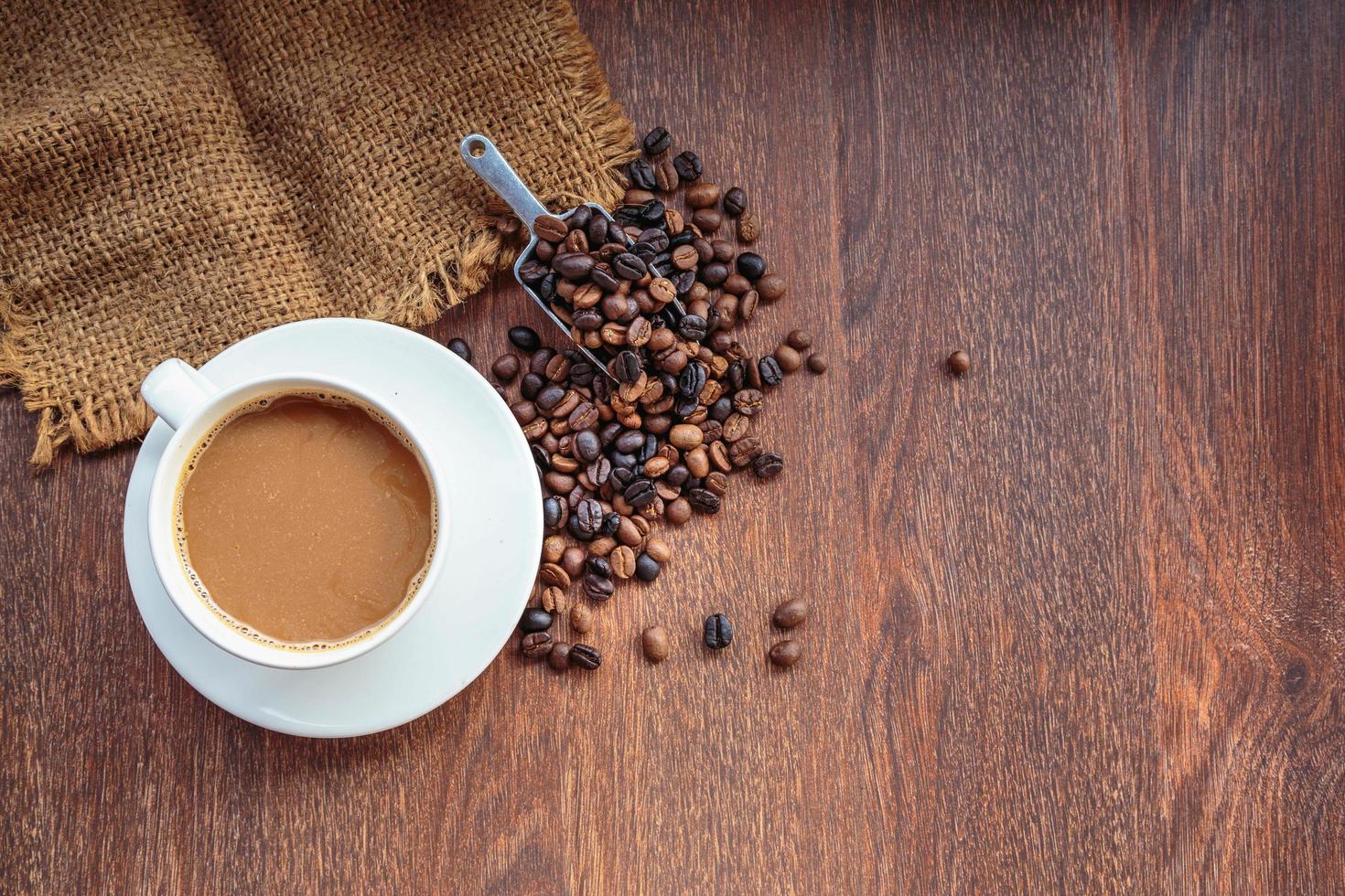 kopp kaffe och kaffebönor i en säck på brun bakgrund, ovanifrån foto