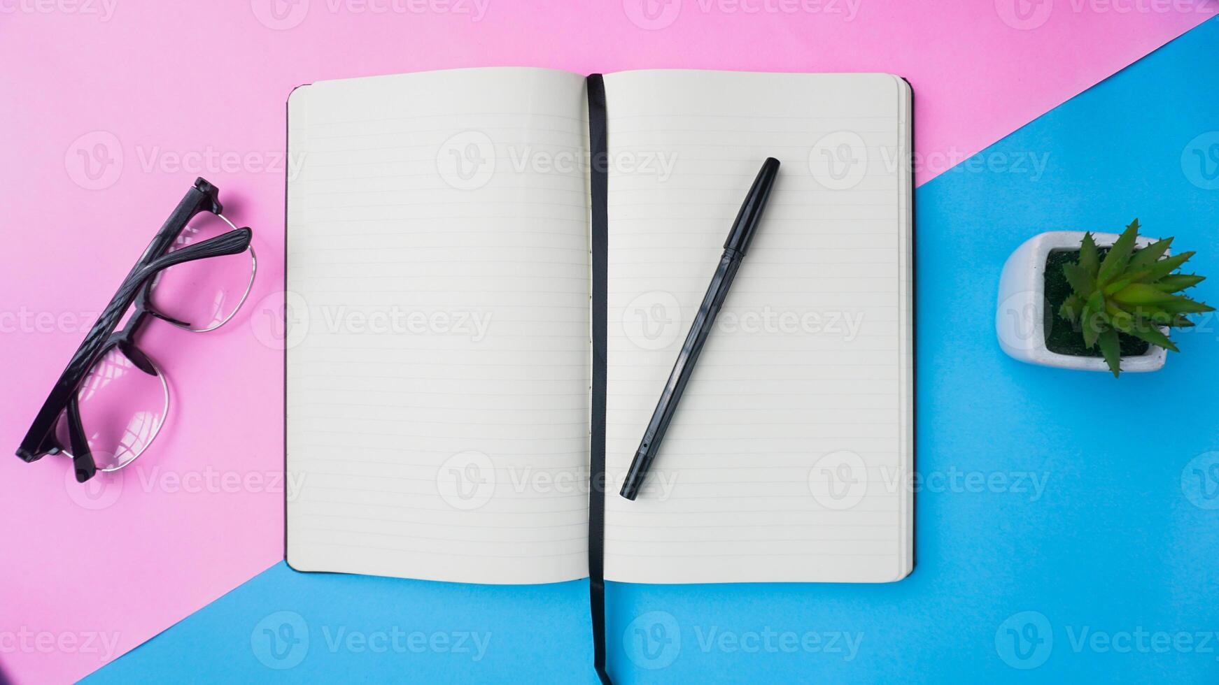 arbetsyta skrivbord med anteckningsböcker, pennor, glasögon, växter, och kaffe på blå bakgrund foto
