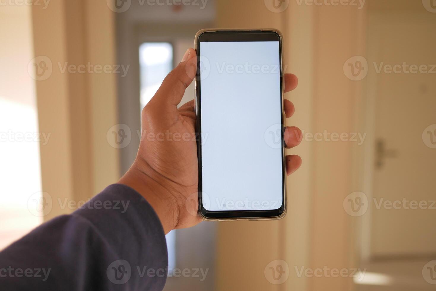 närbild hand använder sig av telefon som visar vit skärm i tömma rum foto