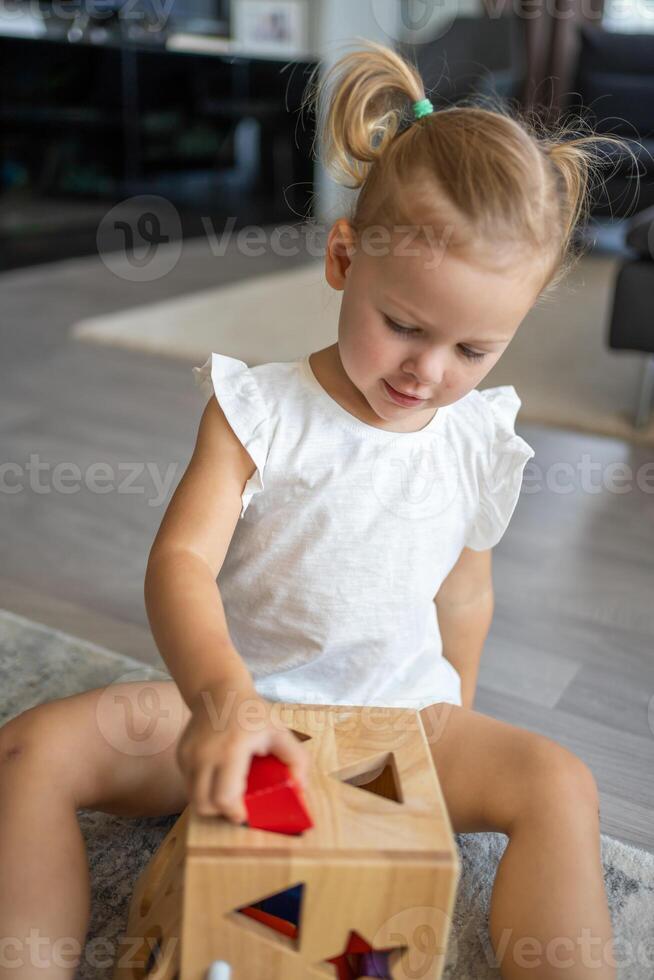 söt caucasian liten flicka spelar på de golv på Hem med eco trä- leksaker. de barn spelar pedagogisk spel. foto