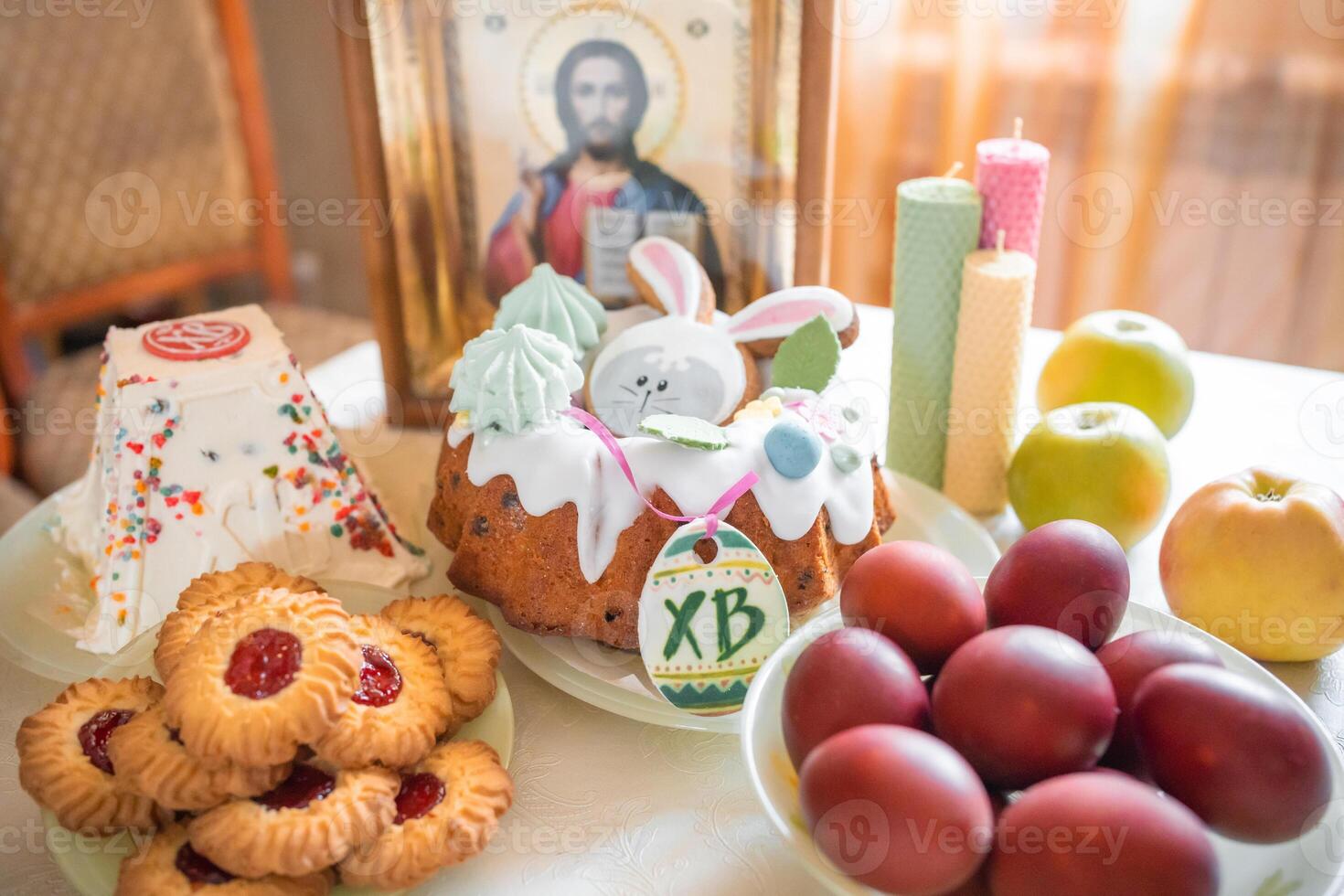 påsk kaka med målad ägg, äpplen och småkakor på tabell i Hem kök. kyrka ikoner och ljus på bakgrund. ortodox religion tema. foto