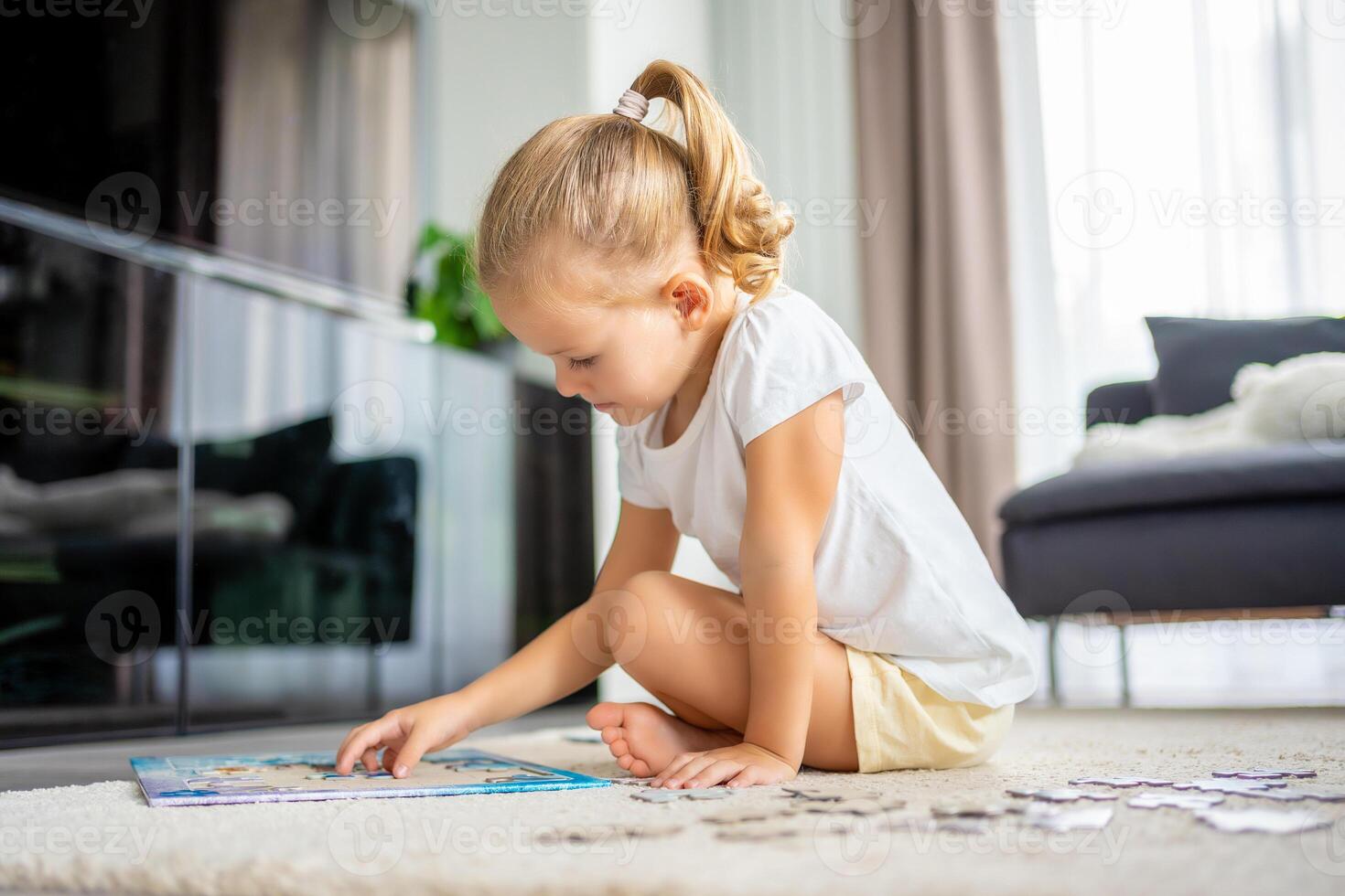 liten blond flicka sitter på Hem på de matta och samlar pussel foto