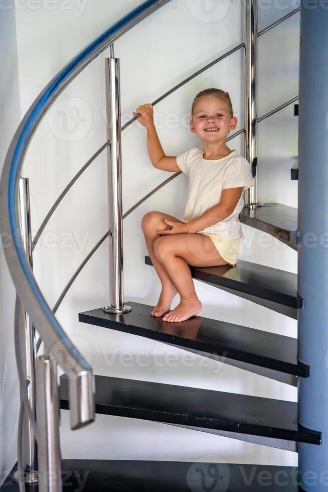 liten barn flicka är Sammanträde ensam på spiral trappa på modern Hem. farlig situation på Hem. barn säkerhet begrepp. foto