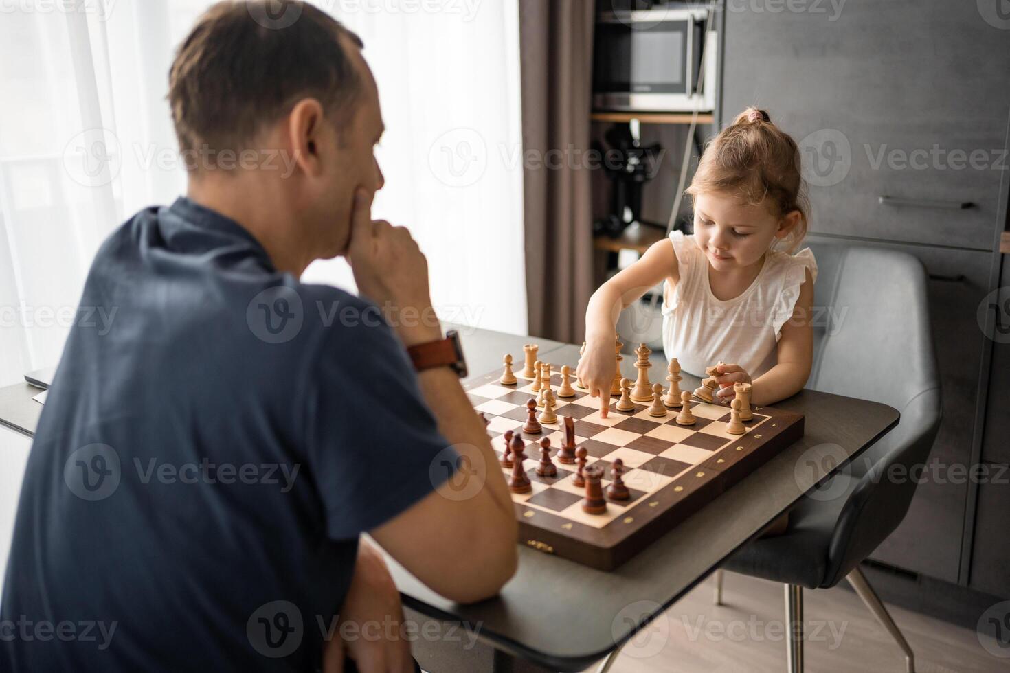 liten flicka spelar schack med henne far på de tabell i Hem kök. de begrepp tidigt barndom utveckling och utbildning. familj fritid, kommunikation och rekreation. foto