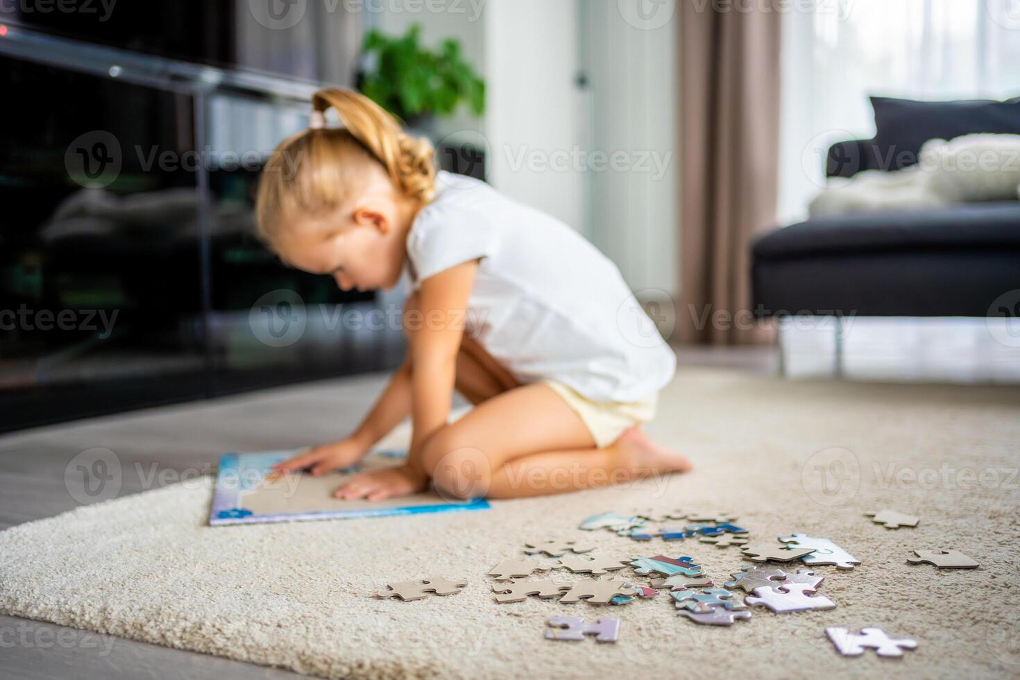 liten blond flicka sitter på Hem på de matta och samlar pussel foto