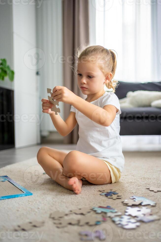 liten blond flicka sitter på Hem på de matta och samlar pussel foto