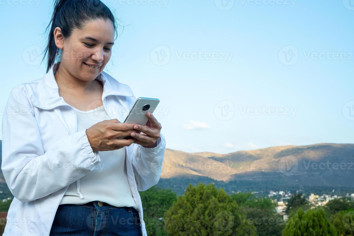 latin kvinna använder sig av henne cell telefon i en parkera. foto