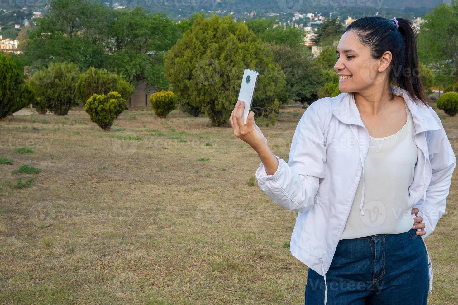 latin kvinna använder sig av henne cell telefon i en parkera. foto