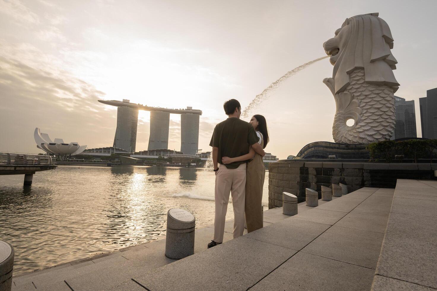 merlion fontän i främre av de marina bukt sandstrand med ung asiatisk par av kärlek turist. foto