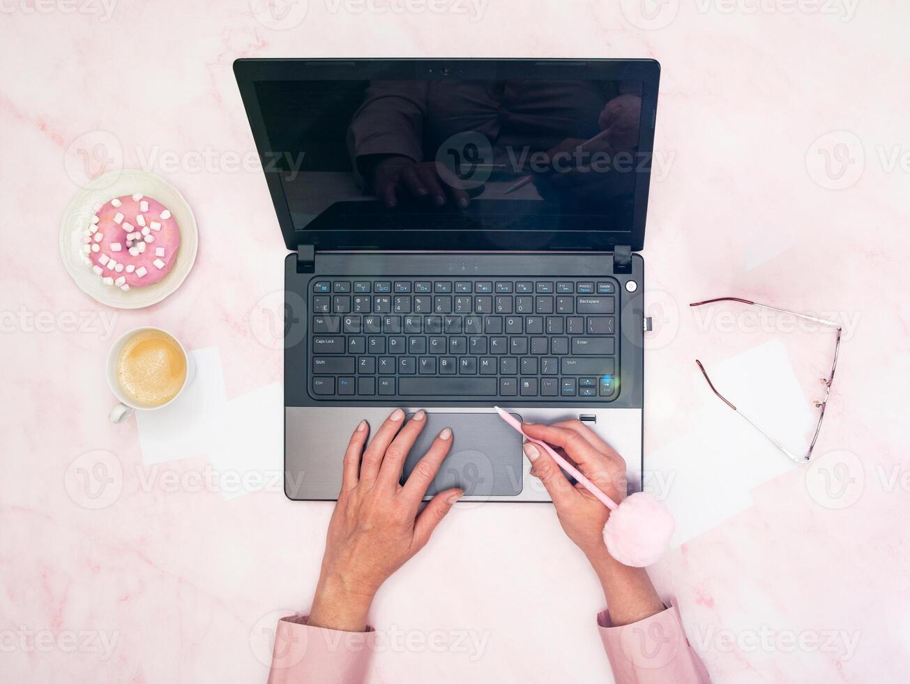 kontor arbetstagare i en rosa skjorta sitter på en bärbar dator, topp visa, nästa till en kopp av kaffe foto